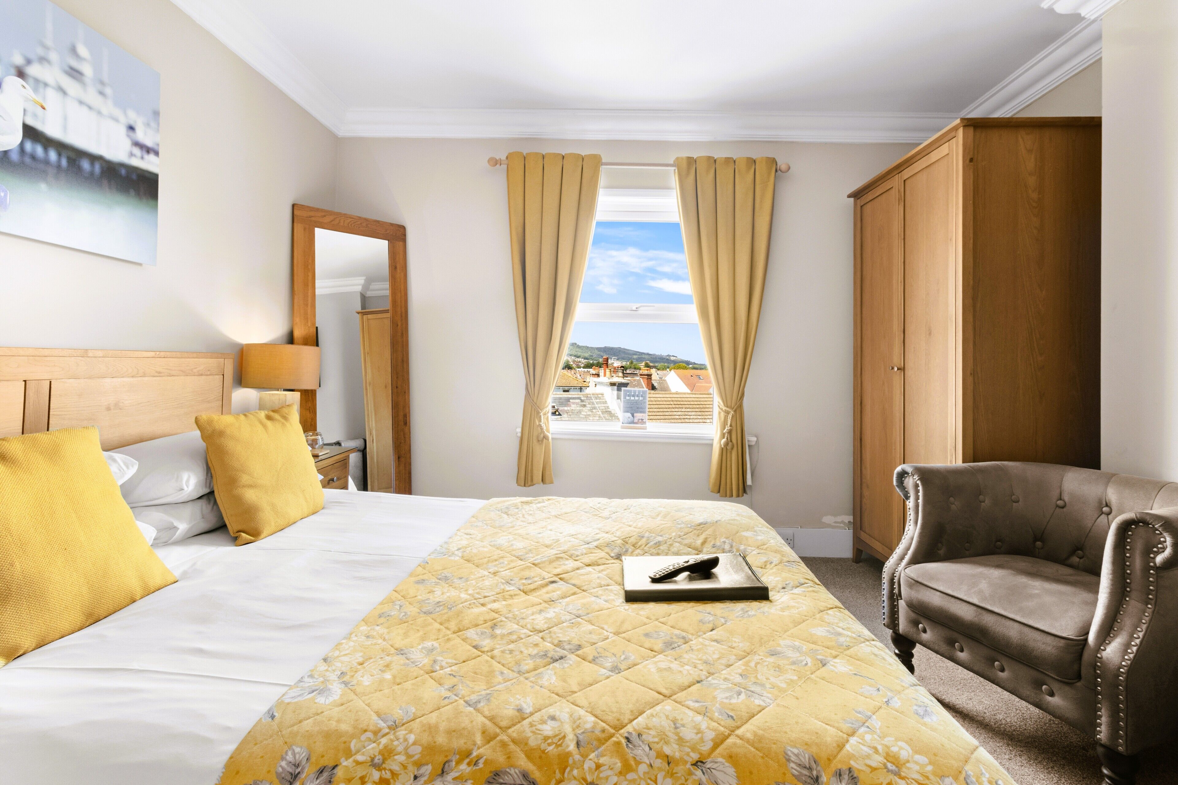 A hotel room with a bed, a wooden wardrobe, a leather armchair, and a window with curtains.