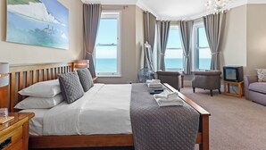 Et hotelværelse med en stor seng, et skrivebord, en stol, et fjernsyn og havudsigt.