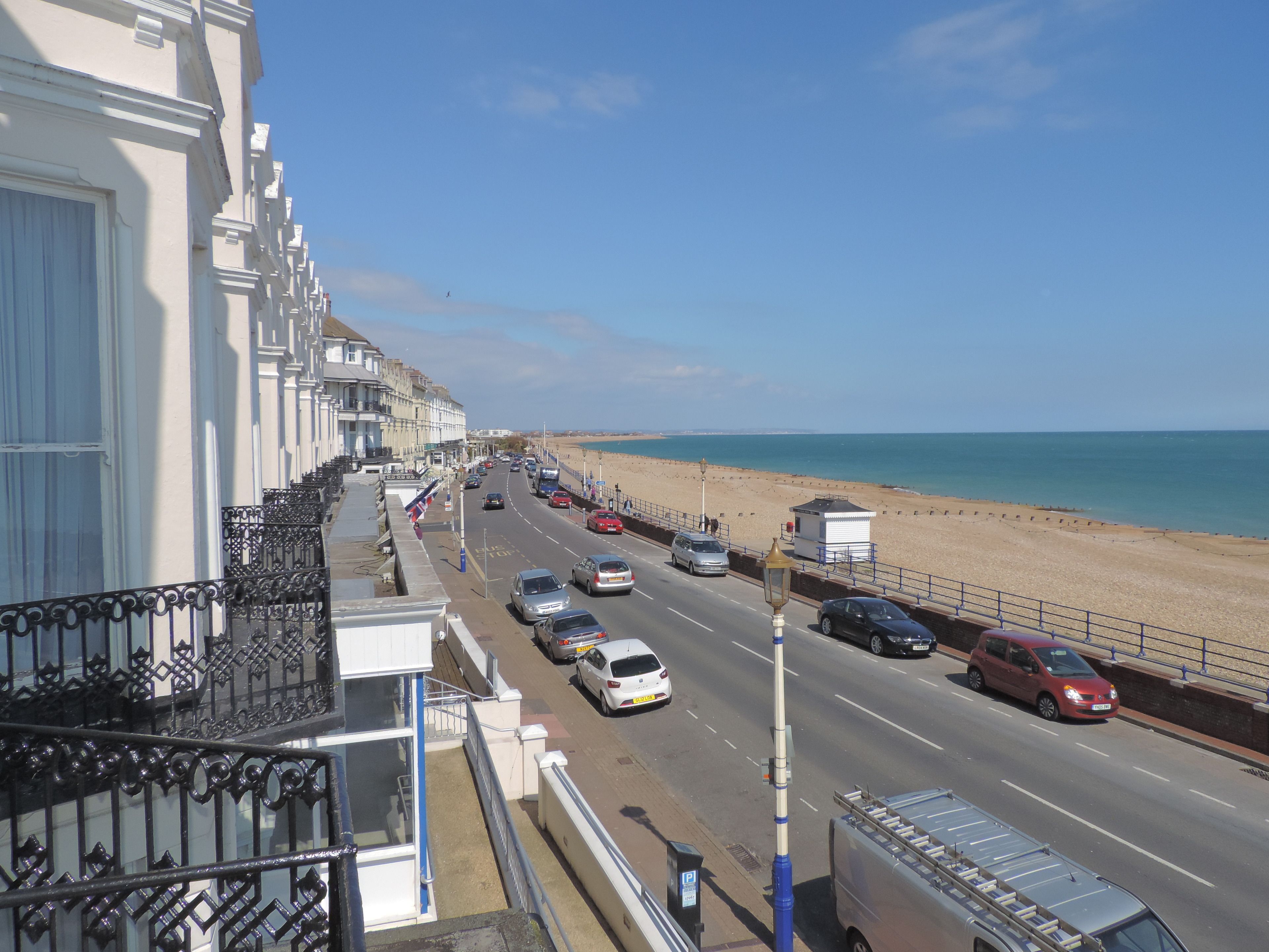 A coastal road with cars, a beach, and white buildings.