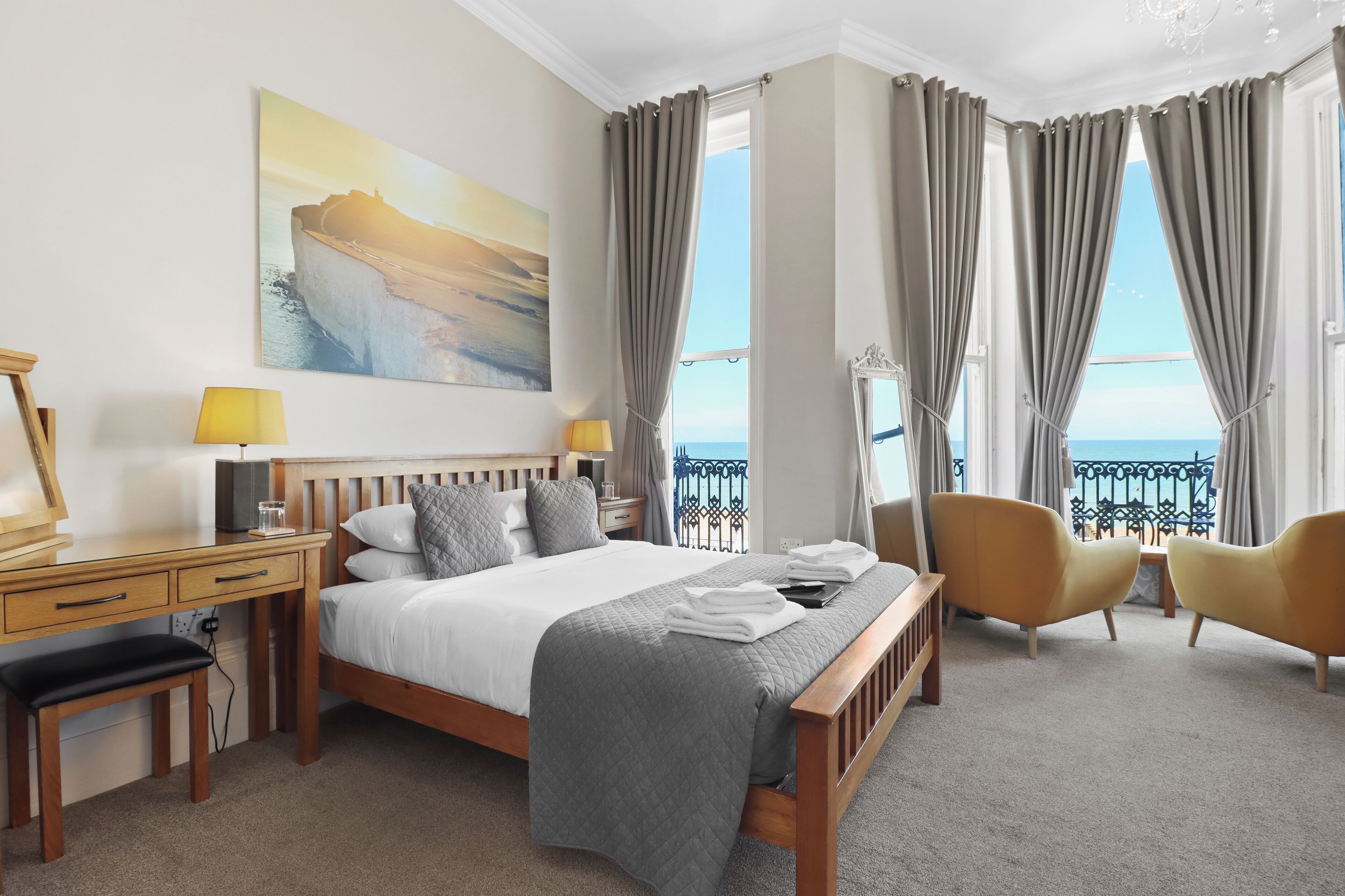 Un cuarto de hotel con una cama grande, un escritorio con lámpara, dos sillones y vista al mar a través de amplios ventanales.