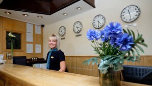 A reception desk with clocks displaying times for New York, London, and Tokyo, and a vase of blue flowers. - The Cathedral Hotel (Lichfield)