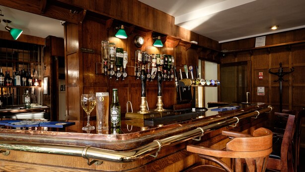 A bar area with wooden paneling, multiple taps, and a variety of bottles. - The Cathedral Hotel (Lichfield)