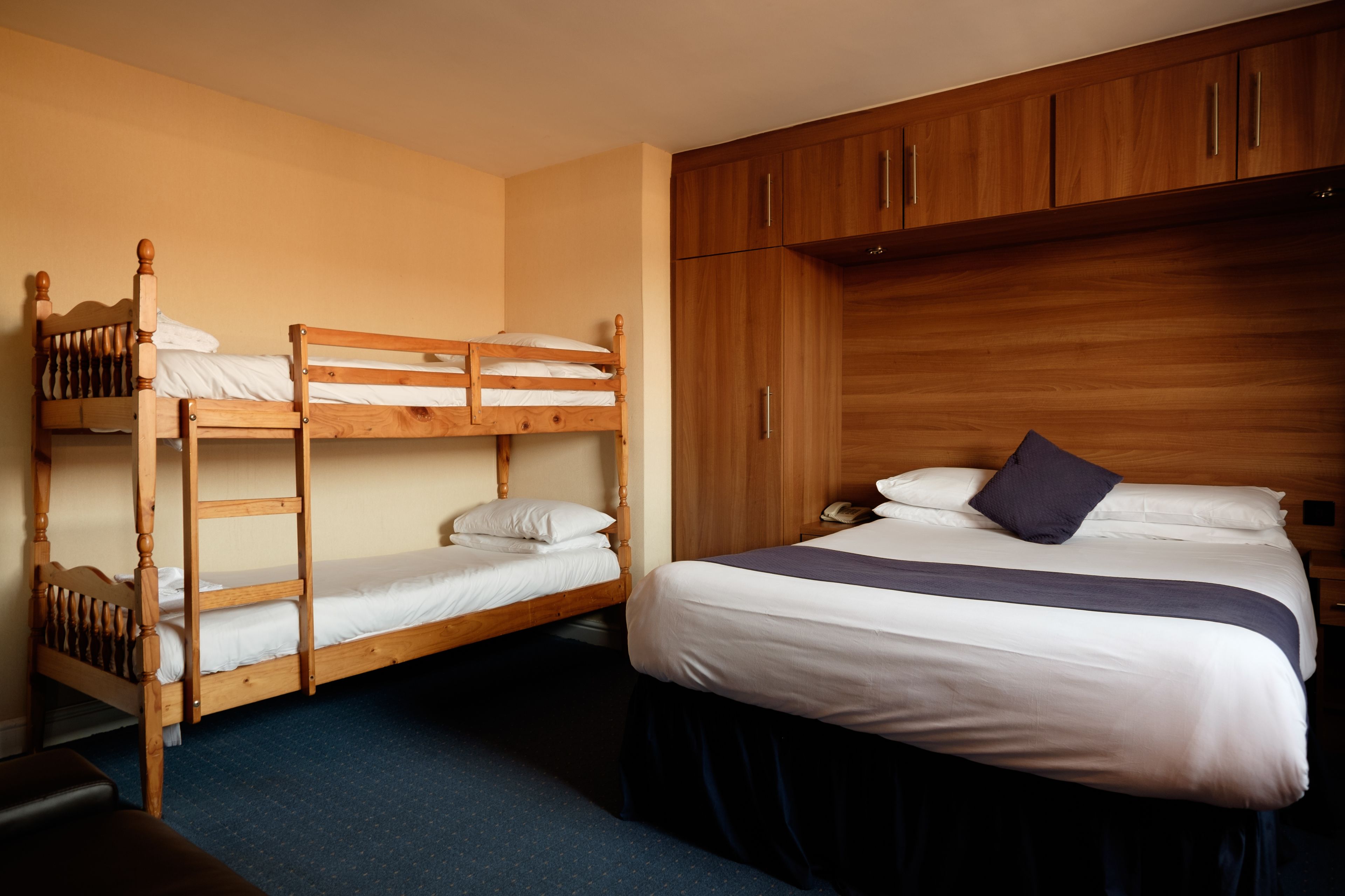 Quarto com beliches, uma cama de solteiro, armários de madeira e um tapete azul.