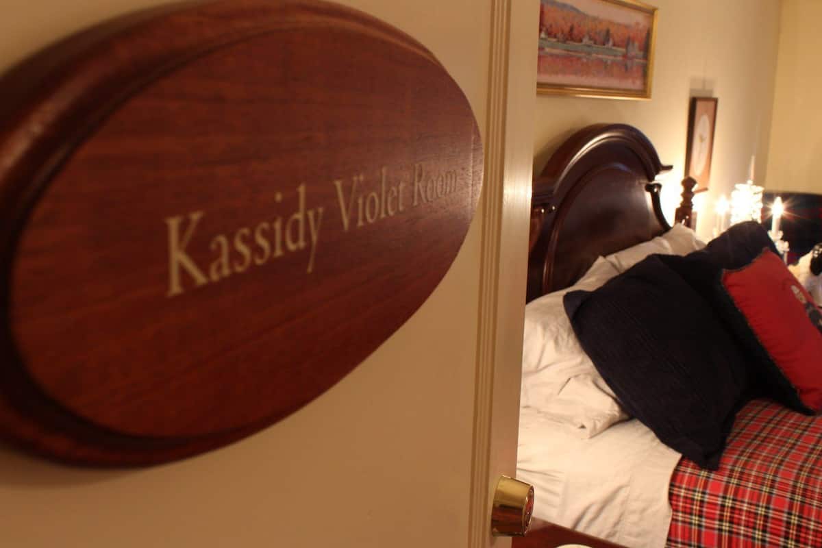 A room with a bed, a door with a nameplate reading "Kassidy Violet Room," and a painting on the wall.