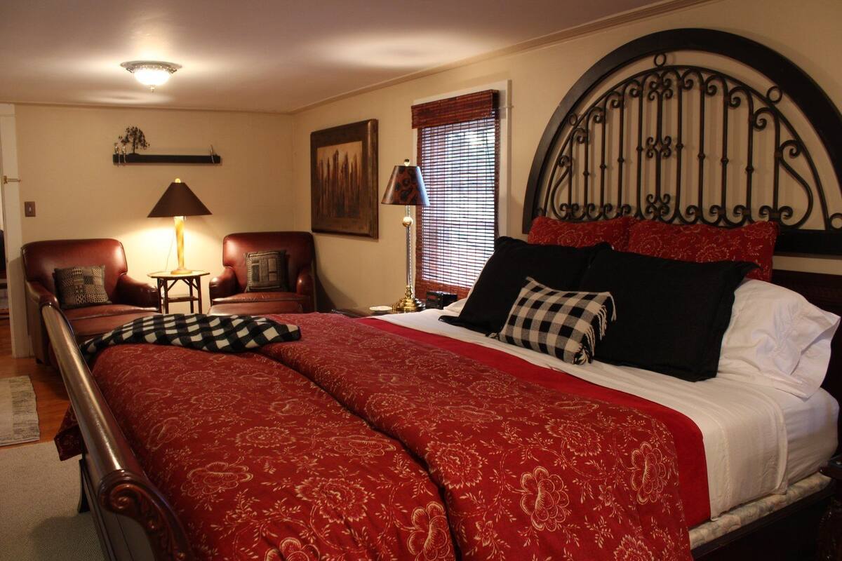 A bedroom with a large bed, two bedside tables, a chair, a lamp, and a window with blinds.