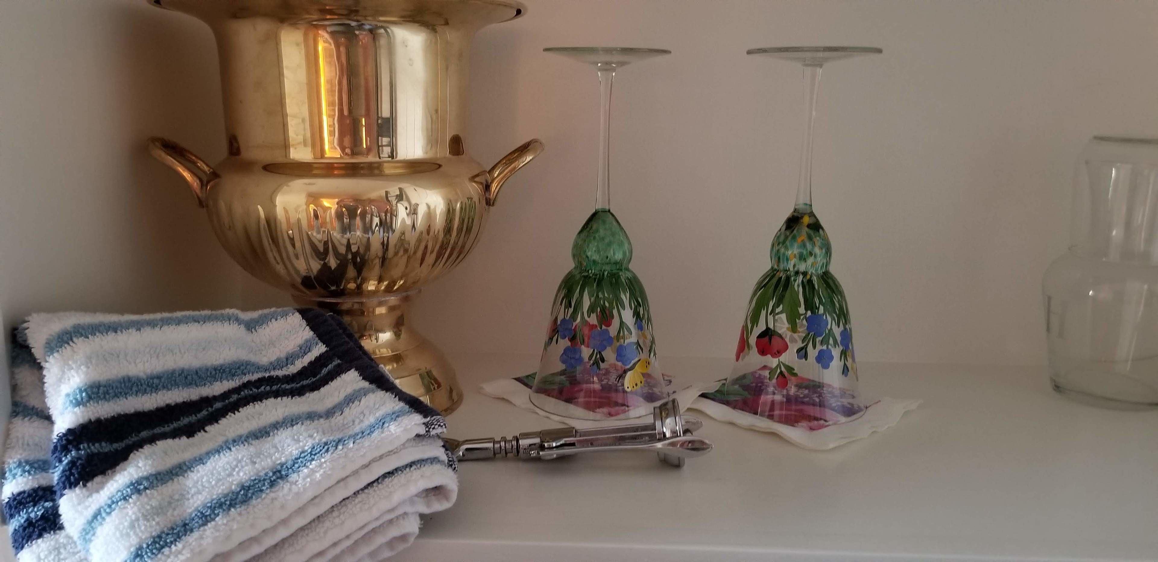 A bathroom with a gold-colored vessel, two glass vases with floral designs, a striped towel, and a pair of scissors.