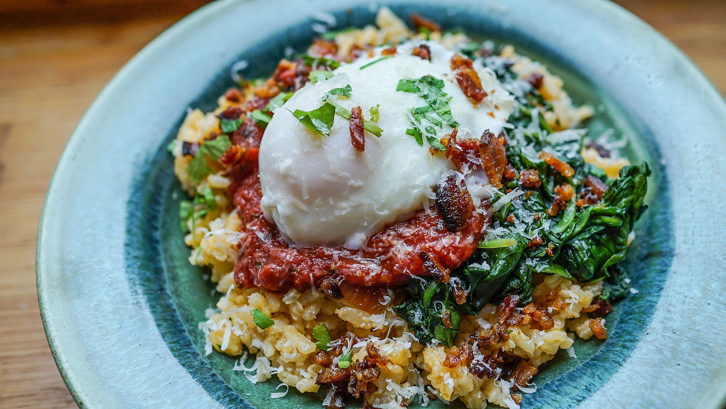 Une assiette contenant un plat composé d’un œuf poché, d’épinards et d’une céréale, peut-être un risotto.