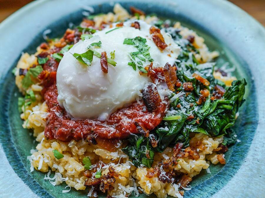 Une assiette contenant un plat composé d’un œuf poché, d’épinards et d’une céréale, peut-être un risotto.