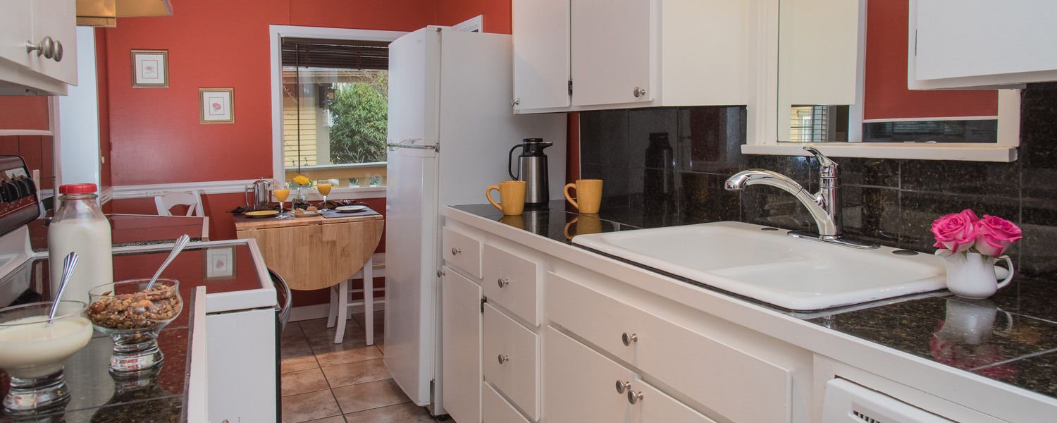A compact kitchen with white cabinets, a sink, and a window with a view of greenery outside.