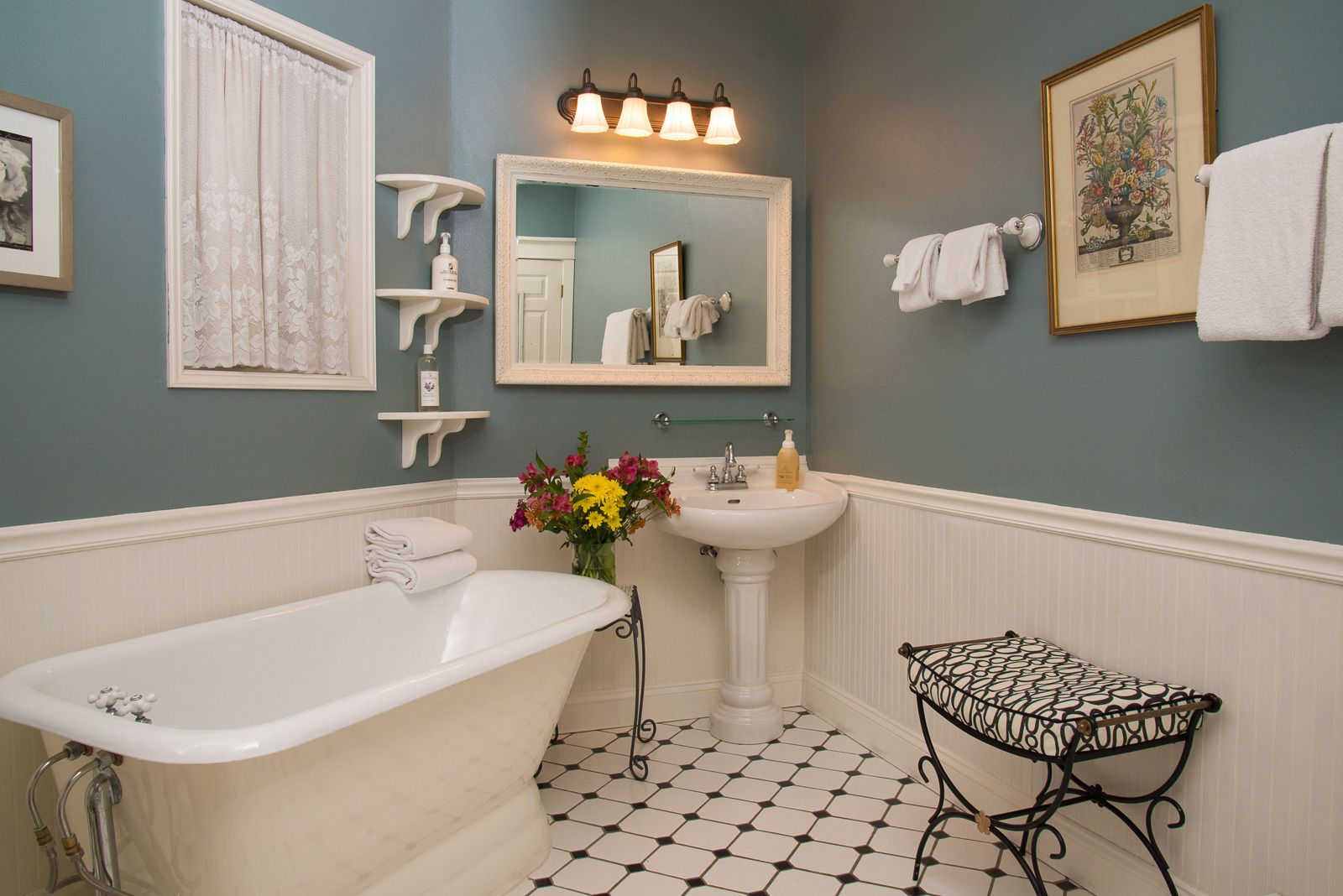 Une salle de bain avec une baignoire sur pieds, un lavabo sur colonne et une petite table à structure métallique.