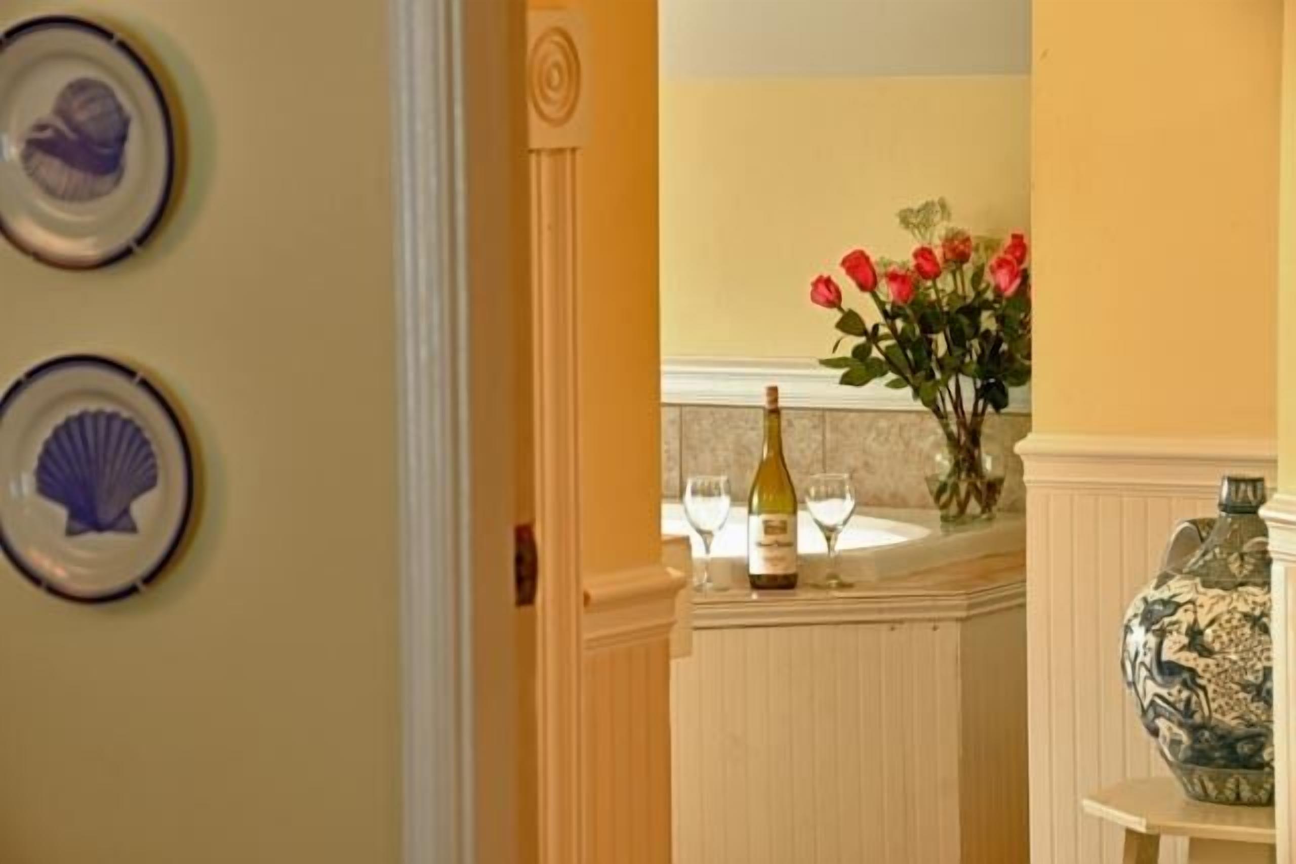 A doorway leading to a room with a wine bottle and glasses on a counter, a vase with red roses, and decorative plates on the wall.