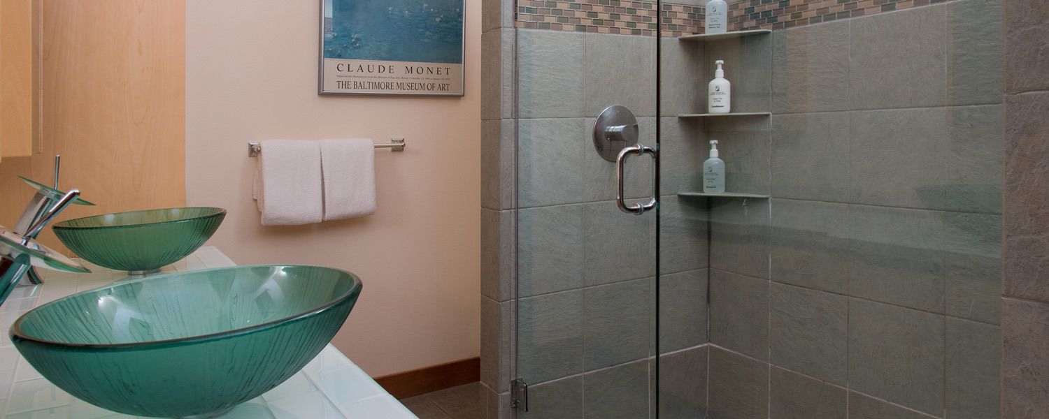 Un baño con lavamanos de vidrio, ducha con puerta de vidrio y un perchero para toallas.