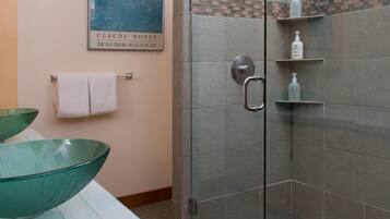 Un baño con lavamanos de vidrio, ducha con puerta de vidrio y un perchero para toallas.