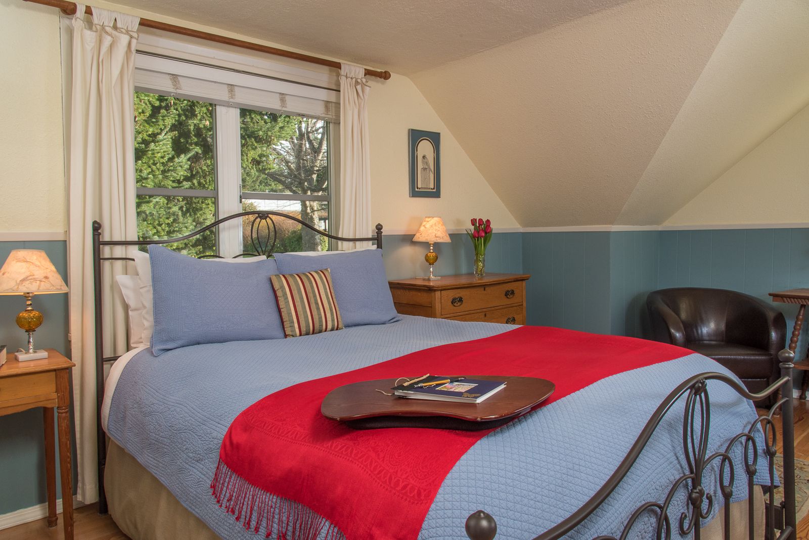 A bedroom with a bed, a nightstand, a chair, a window with curtains, and a wall-mounted picture.