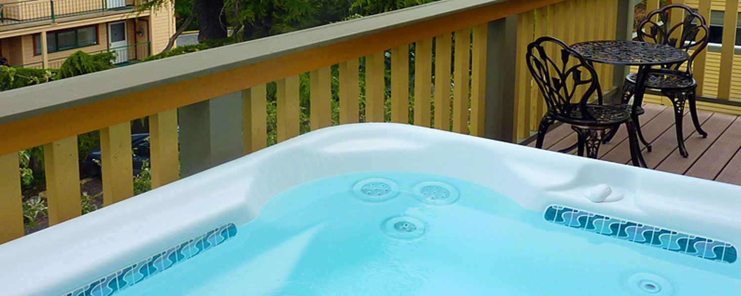 A hot tub on a balcony with a view of a building and a table with chairs.