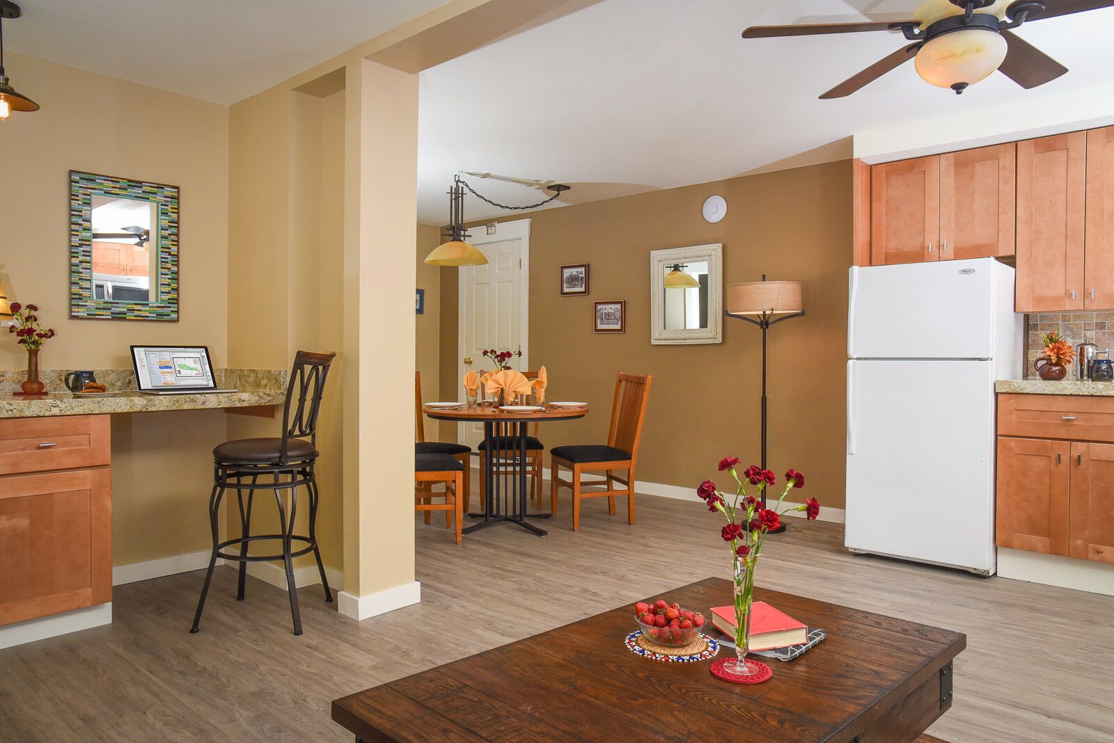A compact kitchen with wooden cabinets, a white refrigerator, and a dining area with a table set for four.
