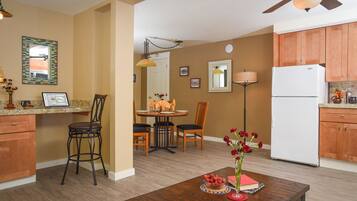 A compact kitchen with wooden cabinets, a white refrigerator, and a dining area with a table set for four.