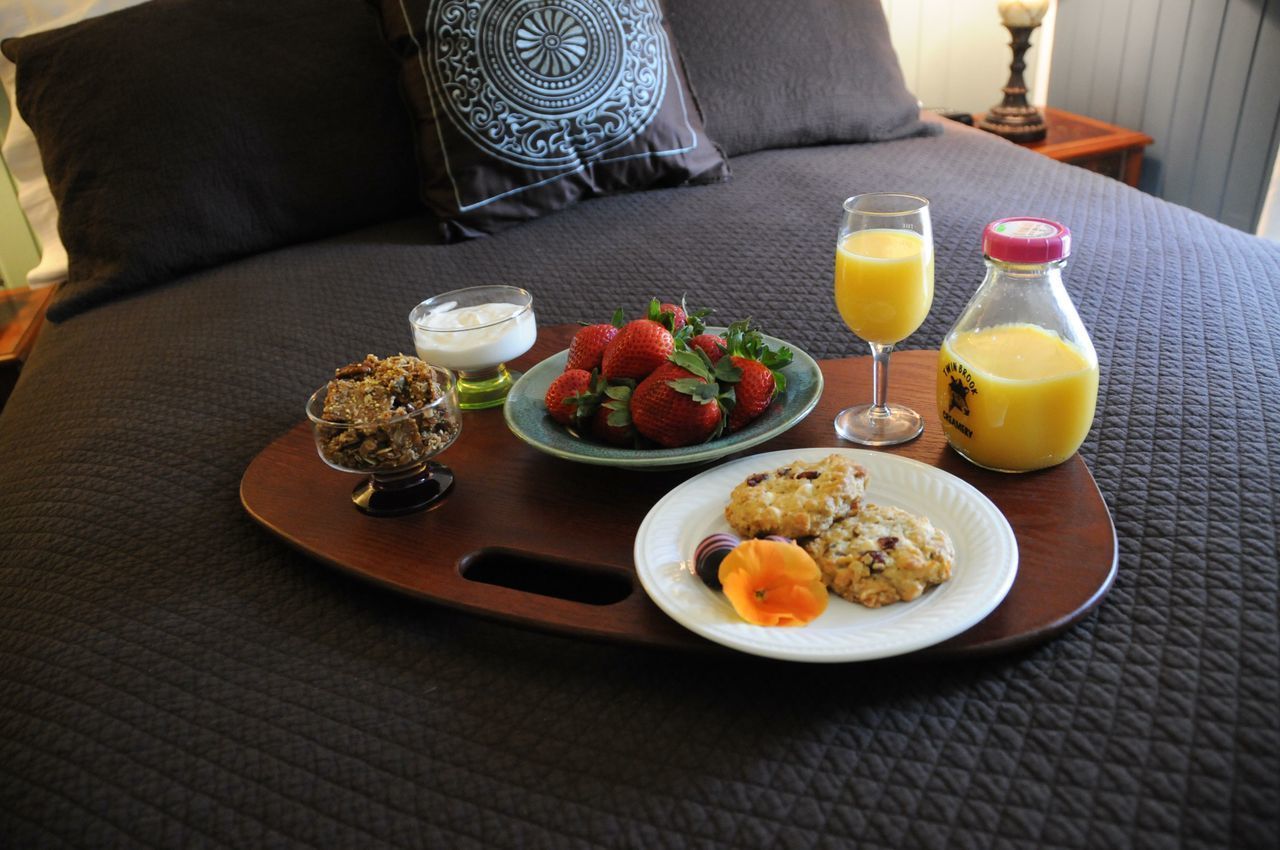 Una bandeja de desayuno en una cama con un plato de fresas, un vaso de jugo de naranja, una botella de jugo, un tazón de yogur y un plato de galletas.