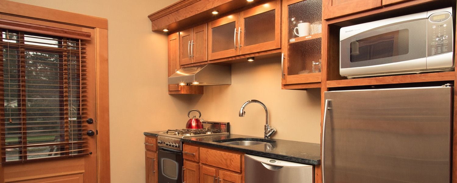 A kitchen with wooden cabinets, a stainless steel refrigerator, a microwave, a sink, and a stove.