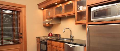 A kitchen with wooden cabinets, a stainless steel refrigerator, a microwave, a sink, and a stove.