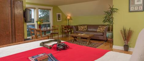 A cozy living room with a large bed, a brown leather sofa, a coffee table, and a dining area with wooden furniture.