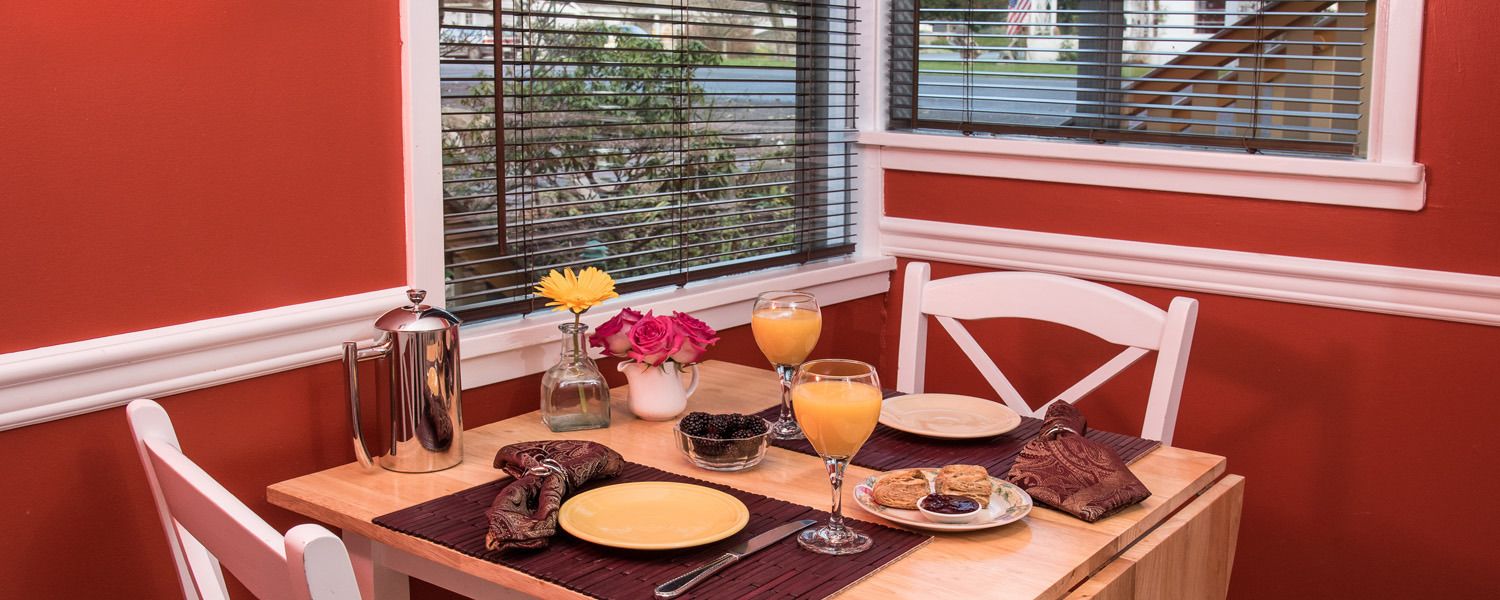 A breakfast table set with a coffee pot, a vase with flowers, a glass of orange juice, a plate with pastries, and a bowl of berries.