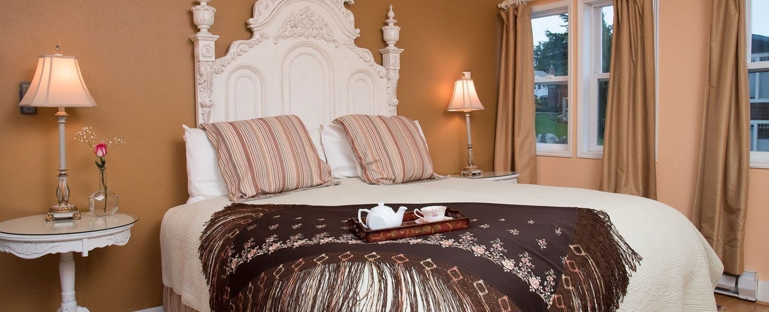 A bedroom with a large bed, two bedside tables, a decorative headboard, and a window with curtains.
