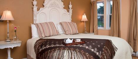 A bedroom with a large bed, two bedside tables, a decorative headboard, and a window with curtains.