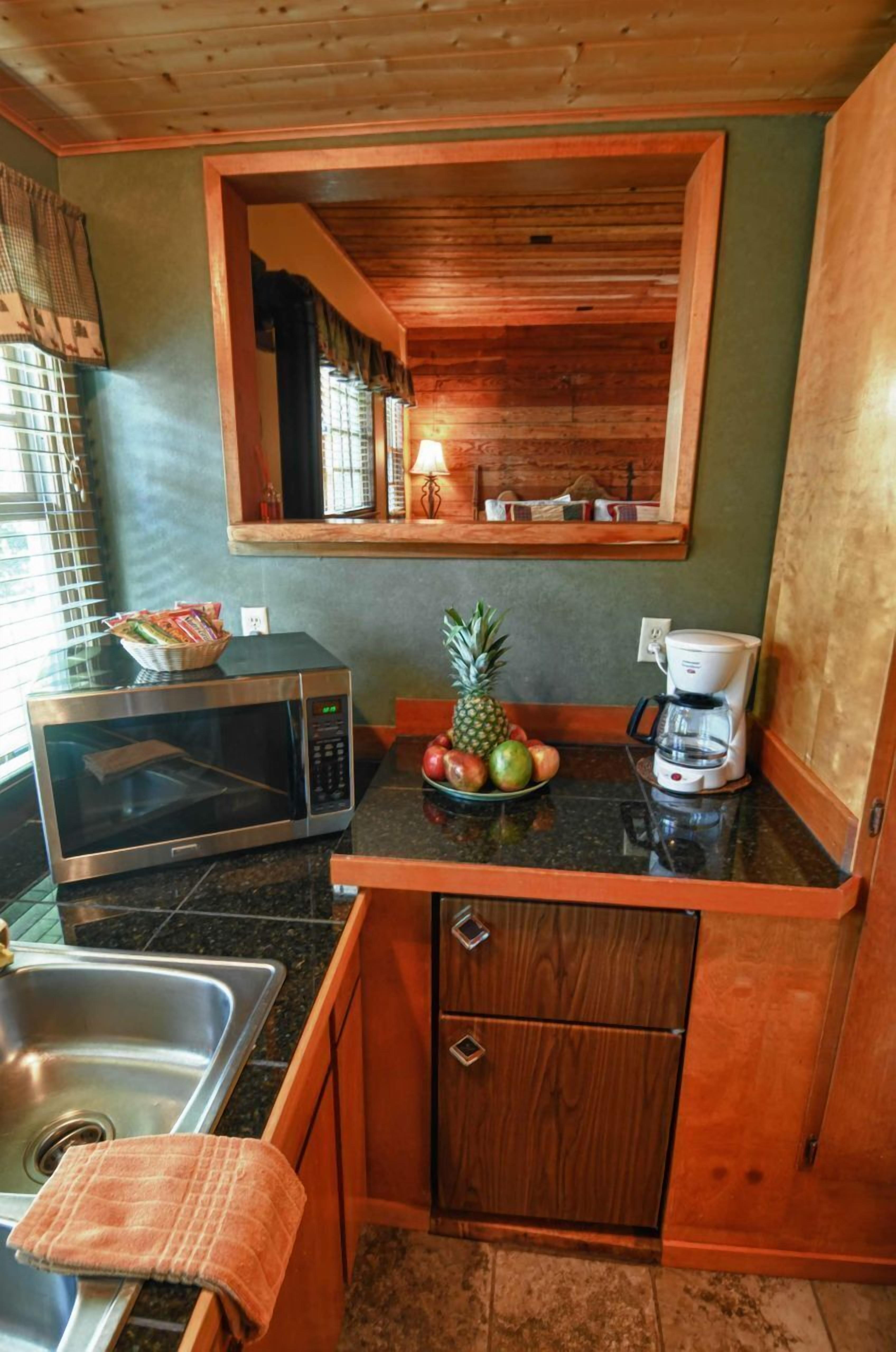 Cocina compacta con microondas, cafetera y frutero sobre la encimera.