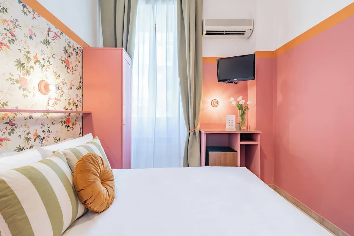 A hotel room with a bed, a desk, a TV, and a window with curtains.