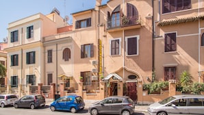 A row of Mediterranean-style buildings with balconies, a street, and parked cars. - Hotel Espana (Rome)