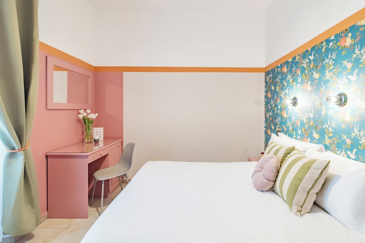 A bedroom with a bed, a desk, a chair, and a mirror.