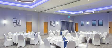 A conference room with multiple tables set for dining, white chairs, and framed artwork on the walls.