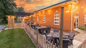 Un espace extérieur aménagé en patio, avec des murs en briques, des guirlandes lumineuses et du mobilier d’extérieur.
