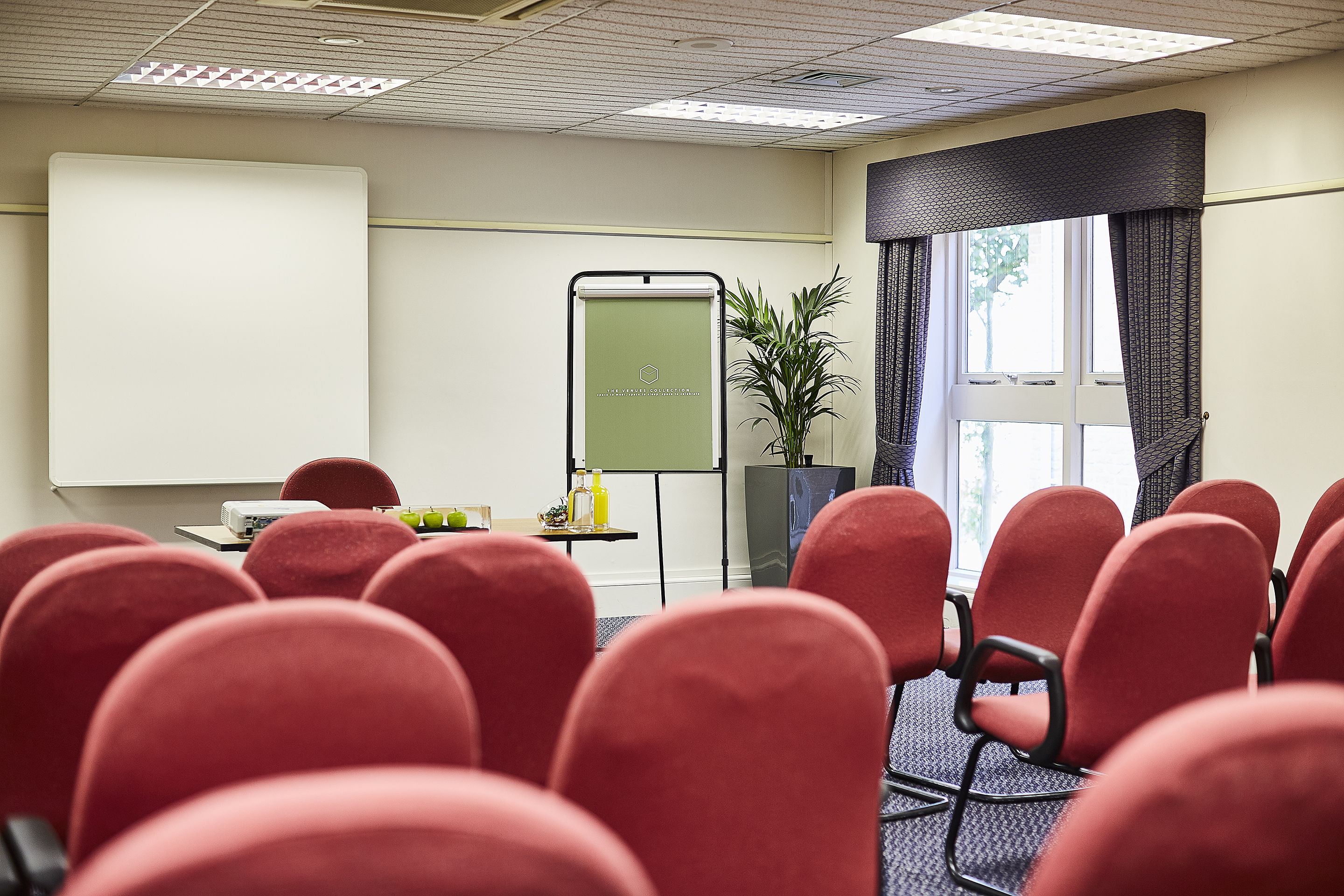 Une salle de conférence avec des chaises rouges, un écran de projection et un tableau de présentation.