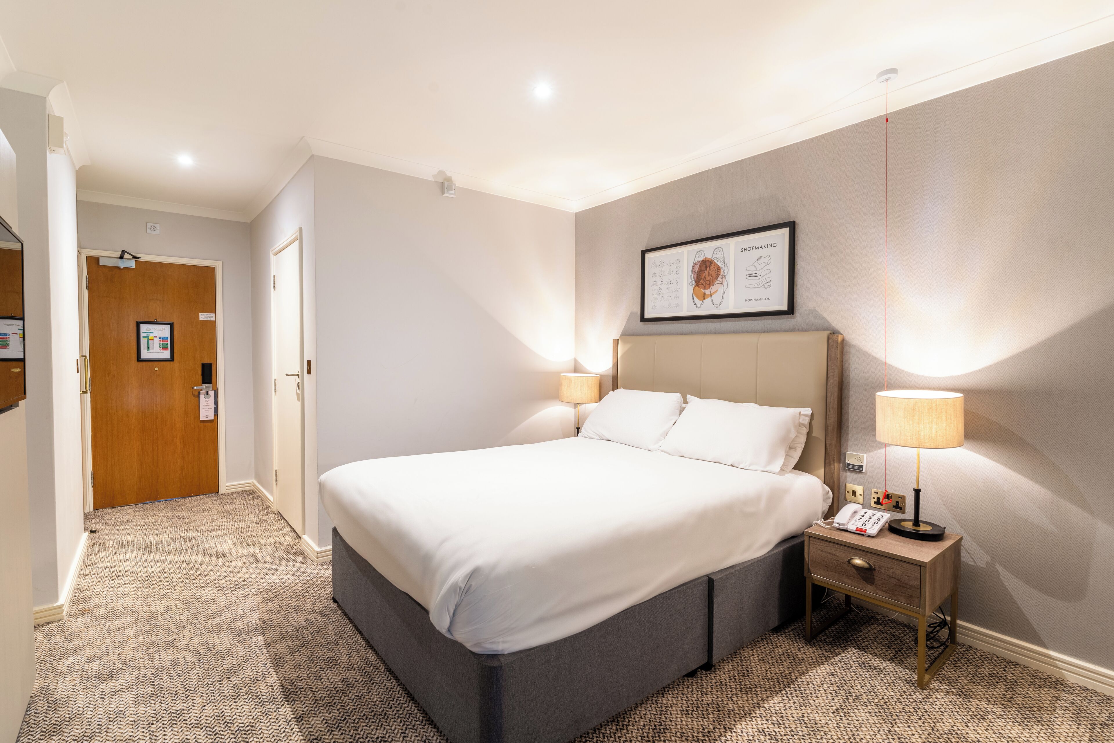A hotel room with a large bed, bedside lamps, a bedside phone, and a framed picture on the wall.
