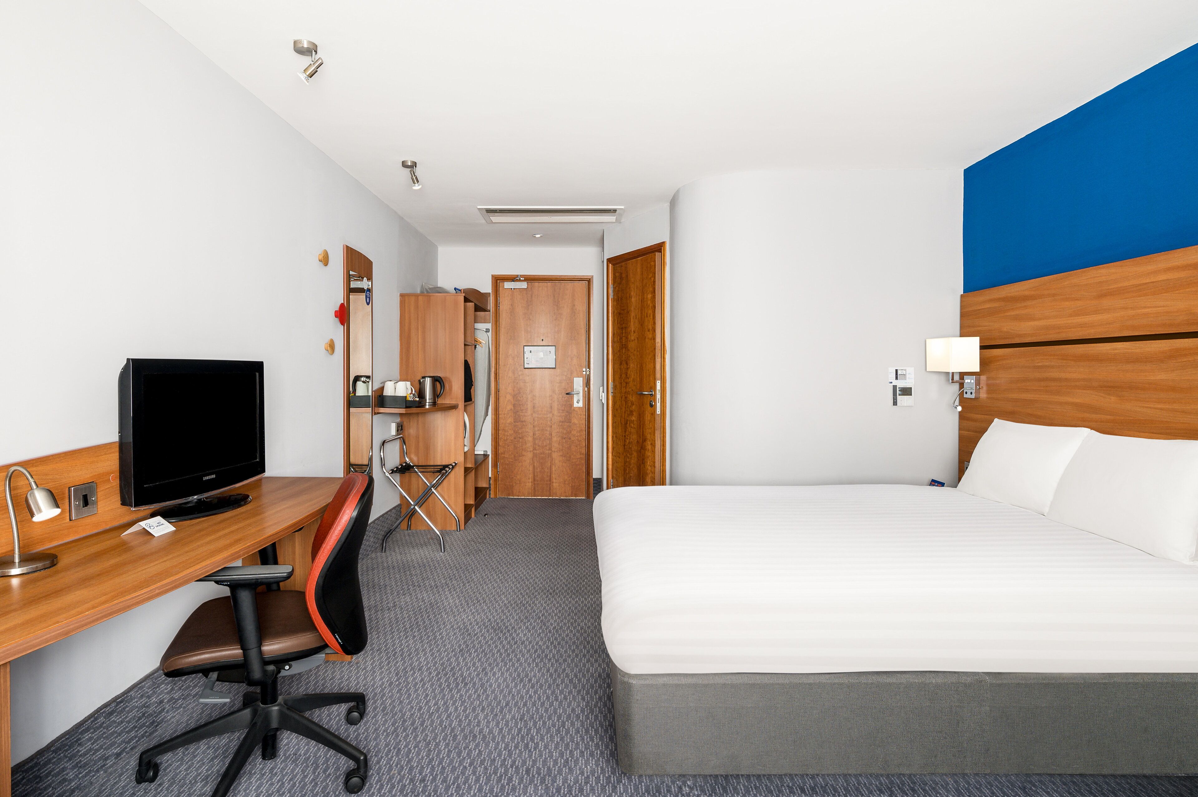 A hotel room with a bed, desk, chair, television, and a bathroom door.