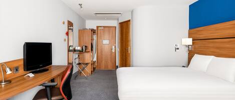 A hotel room with a bed, desk, chair, television, and a bathroom door.