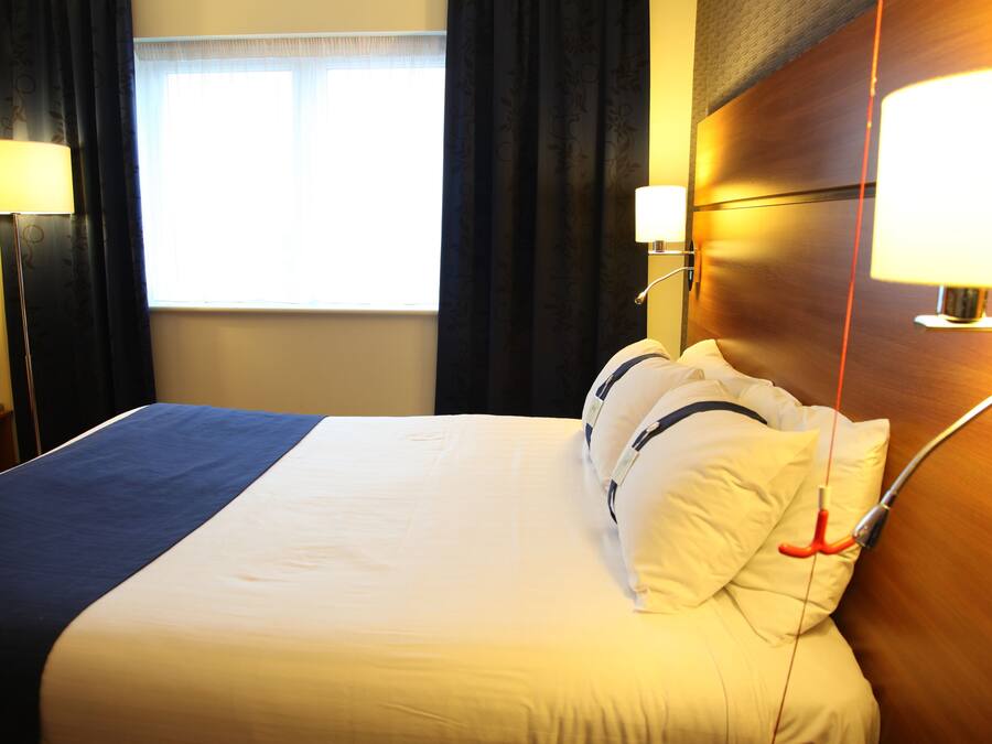 A hotel room with a large bed, two bedside lamps, and a window with curtains.