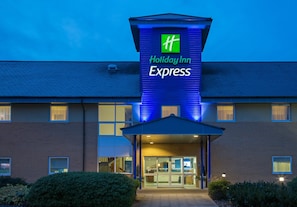 A Holiday Inn Express hotel with a prominent green and white sign, a brick facade, and a well-lit entrance. - Holiday Inn Express Braintree by IHG (Braintree)