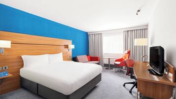 A hotel room with a large bed, a desk with a computer, a chair, and a television.