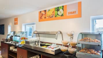 Zona de bufé con diversas opciones de comida, incluyendo frutas, pasteles y bebidas.