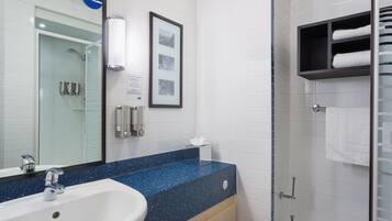 A bathroom with a white sink, blue speckled countertop, framed pictures, and a glass shower enclosure.