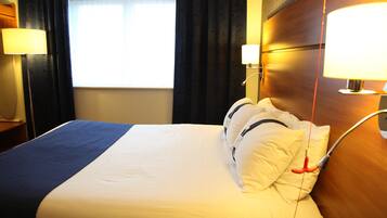 Ein Hotelzimmer mit einem Bett, zwei Nachttischlampen, einem Vorhangfenster und einem hölzernen Kopfteil.