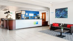 A hotel reception area with a reception desk, a sofa with red cushions, and a coffee table with a plant. - Holiday Inn Express Braintree by IHG (Braintree)