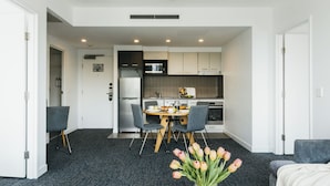 A modern kitchen with white cabinets, a microwave, and a refrigerator. There is a dining table with chairs and a vase of flowers. - Quest Mascot Serviced Apartments (Mascot)