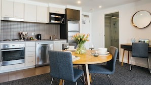 A modern kitchen with white cabinets, stainless steel appliances, and a dining area with a round table and chairs. - Quest Mascot Serviced Apartments (Mascot)