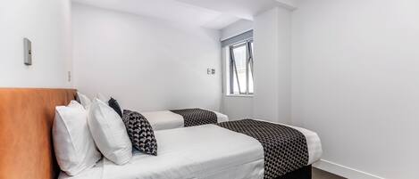 Ein modernes Hotelzimmer mit zwei Betten, einem Holzkopfende und einem Fenster mit Jalousien.