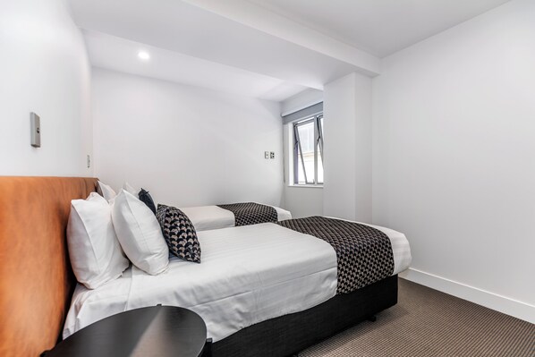 A modern hotel room with two beds, a wooden headboard, and a window with blinds.
