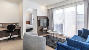 A modern hotel room with a desk, a flat-screen TV, a sofa, and a large window with curtains. - Quest Newmarket (Auckland)